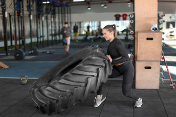 Young muscular woman flipping heavy tire in gym