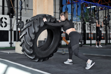 Young muscular woman flipping heavy tire in gym
