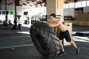 Young muscular man flipping heavy tire in gym