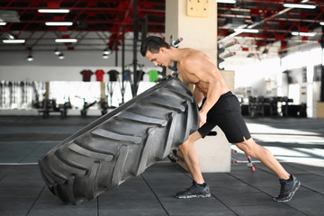 Fototapeta na wymiar Young muscular man flipping heavy tire in gym