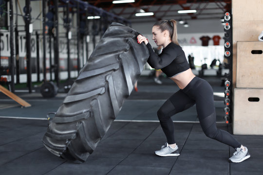 Young muscular woman flipping heavy tire in gym