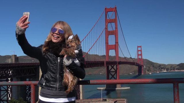 Attractive Woman Tourist taking a Selfie Picture with her cute pet dog at the Golden Gate Bridge