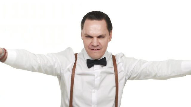 Portrait of artistic energetic man wearing white shirt and bow tie having fun while dancing and partying, over white background. Concept of emotions