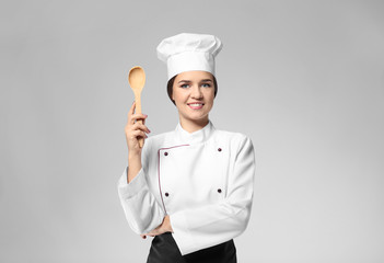 Portrait of female chef with wooden spoon on grey background
