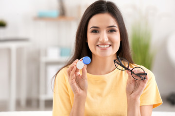 Young woman holding contact lens case and glasses on blurred background