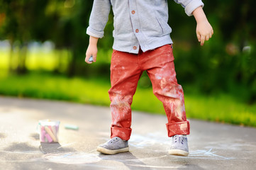 Obraz premium Close-up photo of little kid boy drawing with colored chalk on asphalt.