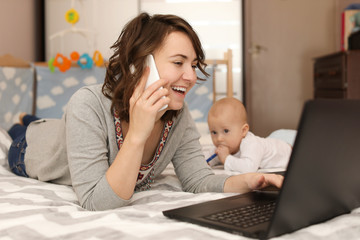 Young mother with baby working on bed at home