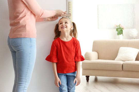Mother measuring height of little girl near door