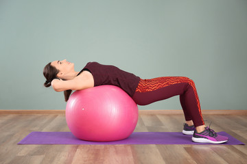 Beautiful young woman doing fitness exercise with ball at home