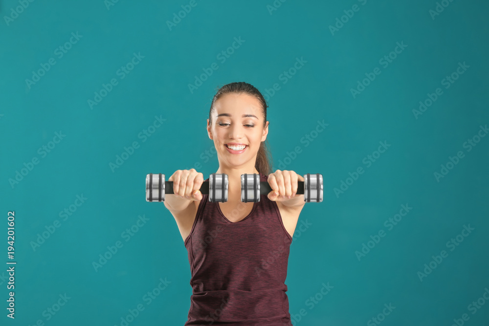 Wall mural Beautiful young woman doing fitness exercise with dumbbells on color background