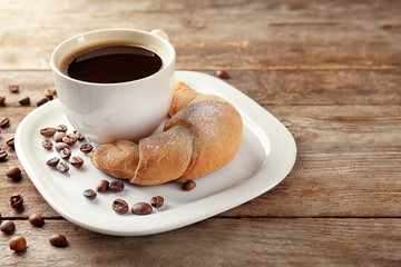Tasty crescent roll and cup of coffee on wooden background