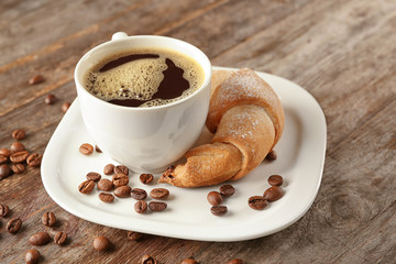 Tasty crescent roll and cup of coffee on wooden background