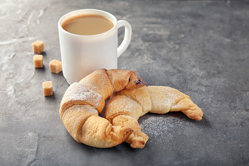 Tasty crescent rolls and cup of coffee on grey background