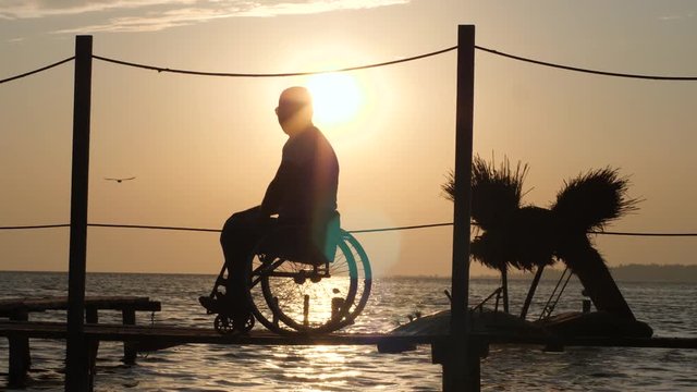 gracious female with happy handicapped look into distance and shows his hand tohorizon on background of orange afterglow at over river at weekend