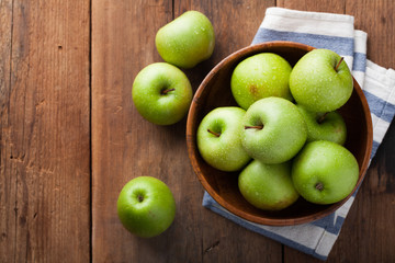 Ripe green apples in a wooden bowl on an old rustic table. Useful fruits on wooden background. Top view with copy space