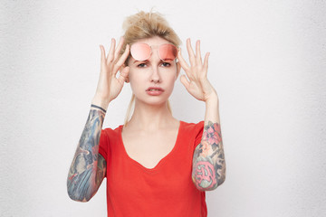 Portrait of young uncertain and unassured pretty blond girl, wears red casual t-shirt and ret...