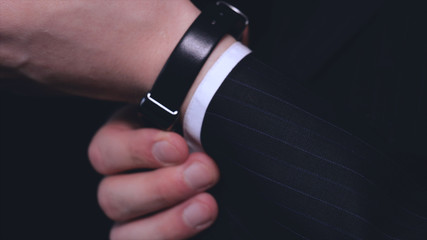 Businessman in suit, touching watch, black background.
