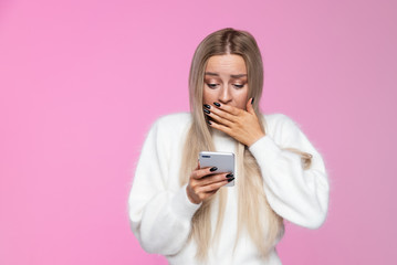 Fototapeta premium Anxious woman covers mouth in shock, holding and looking at mobile smart phone, surprise reaction on her face. Awkwardness gestures, expression concept. Isolated 