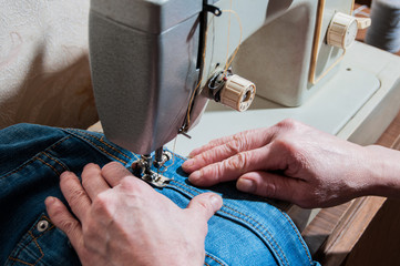 hands of an elderly seamstress working with jeans on a sewing machine