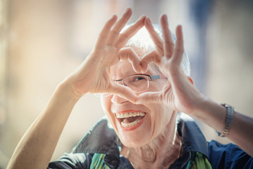 Cute senior old woman making a heart shape with her hands and fingers - obrazy, fototapety, plakaty