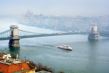 Naklejka premium Danube river in fog, sightseeing boat passing under Chain Bridge, Budapest