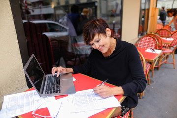 middle aged female student using laptop for writing a research work. Woman sitting at red table in...