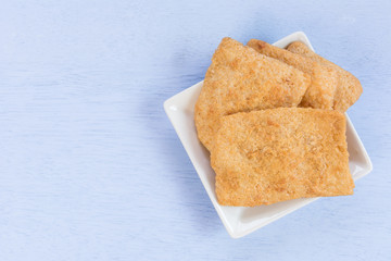 deep fried rice crackers with flossy pork in a ceramic plate on light blue wooden background with copy space, top view. thai style delicious snack.