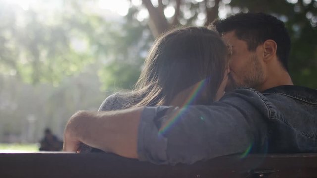 Happy young couple share a kiss on a park bench, in slow motion 