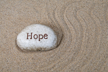Fototapeta na wymiar hope text engraved on a rock in beach sand with swirl design