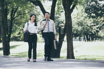 Happy Asian business man and woman walking and talking in the public park after finish work.