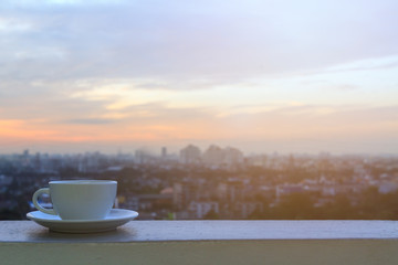 White coffee cup put on sky terrace border with blurred morning city scape and sunrise effect, Selective focus and copy space