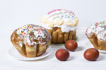 Easter cake with sugar glaze and painted eggs on white wooden background.
