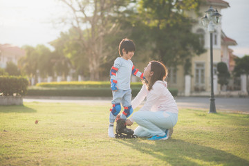 Asian mother helping her son putting his roller skates on enjoying time together in the park