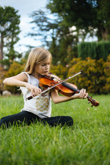 Girl sitting in green grass playing violin