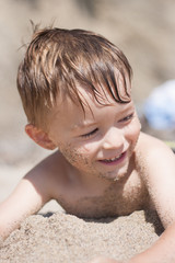 Little caucasian boy laying on the beach with sand on his face and chest