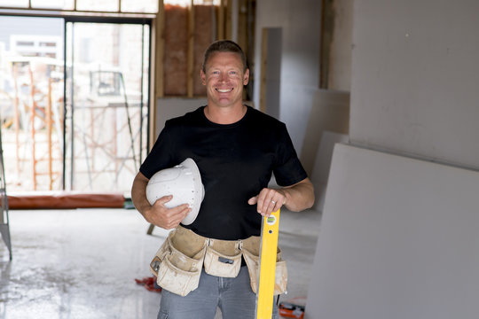 attractive and confident constructor carpenter or builder man with protective helmet posing happy working at industrial construction site