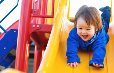 Happy toddler boy playing on a slide at a playground