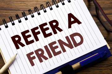 Hand writing text caption inspiration showing Refer A Friend. Business concept for Referral Marketing Written on notebook note paper, wooden background with glasses pen and marker.