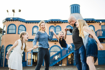 Family of five laughing and swinging the youngest daughter between mom and dad on the boardwalk