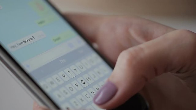 Woman is writing messages on her smartphone, close up. Young lady with beautiful manicure holding brand-new device her hand and typing greetings to her friend be her finger, pushing vitrual buttons.