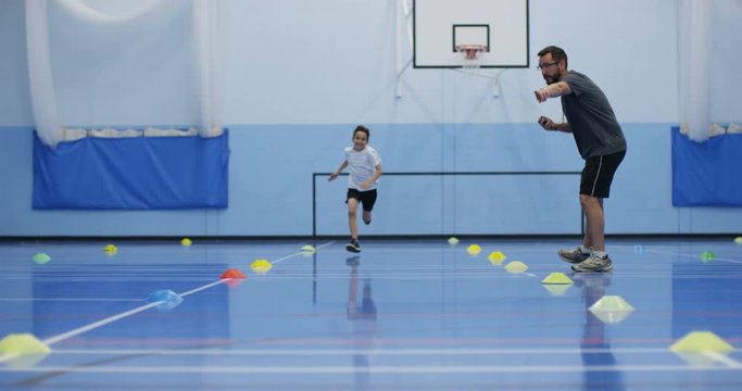 4K Sports teacher coaching young boy, running laps & working hard in school gym