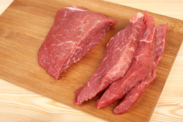 Fototapeta premium Raw beef piece and slices on wooden cutting board