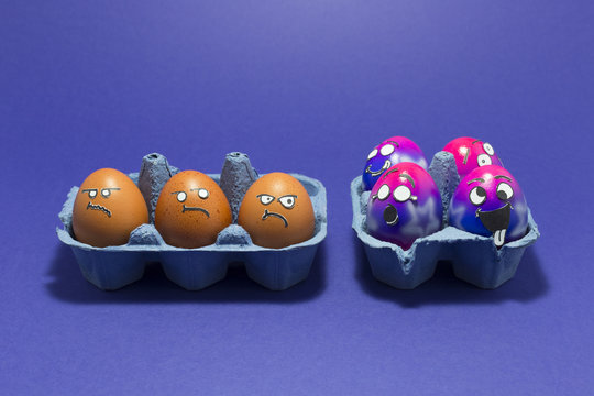 Group of colorful painted Easter eggs with funny cartoon style faces and group of grumpy looking brown eggs in light blue egg boxes on purple background