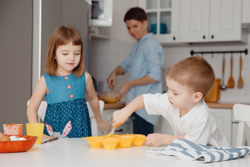 Young family cooking in the kitchen. Happy children, sister and brother smile, laugh, lubricate the baking cups. Concept team work.