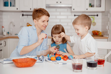 Mom and children, son and daughter paint their eggs with colors. Happy family is preparing for Easter.