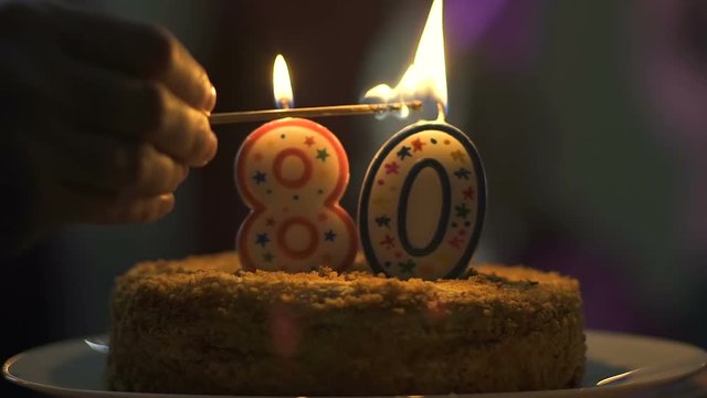 Hand lighting candles birthday cake, 80 anniversary celebration, tasty dessert