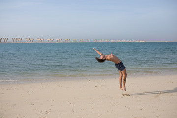 Fototapeta na wymiar Young man doing somersault on the beach.