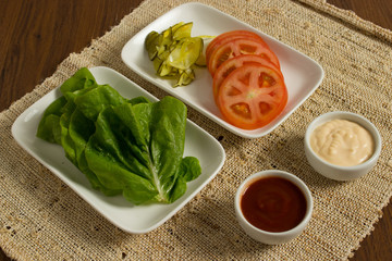 Ingredients for cooking burgers, tomatoes, greens, pickles, ketchup, cheese,  over wooden background