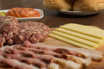 Ingredients for cooking burgers. Raw ground beef meat cutlets on wooden chopping board, cheese, bun,  over wooden background
