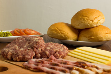 Ingredients for cooking burgers. Raw ground beef meat cutlets on wooden chopping board, cheese, bun,  over wooden background